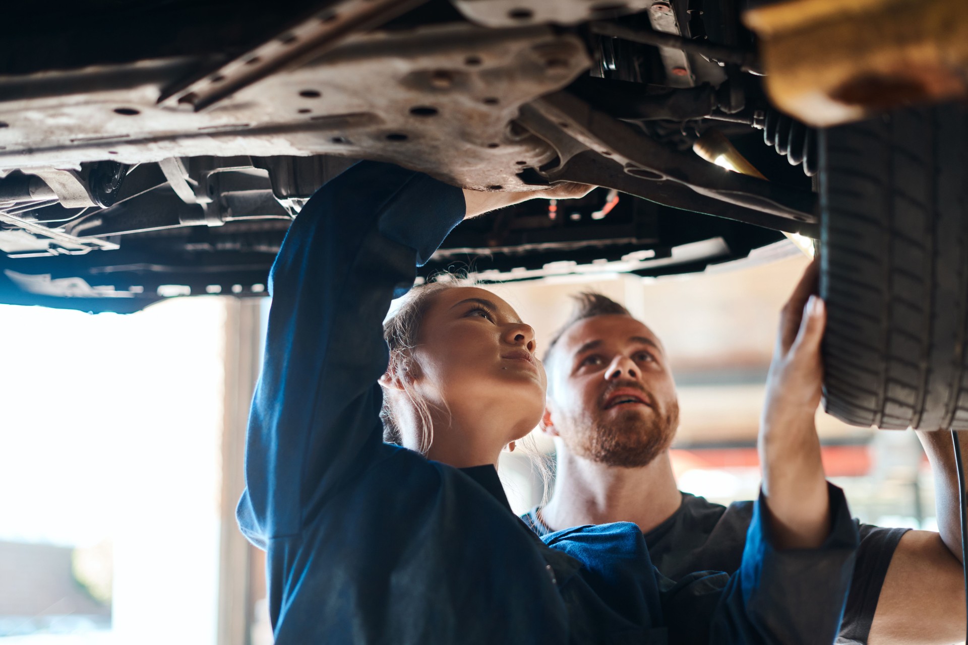 Aufnahme von zwei Mechanikern, die unter einem Auto in einer Autowerkstatt arbeiten